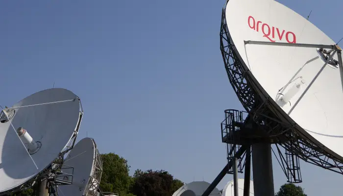 Ground station satellite dishes pointing to the sky. One dish has the words Arqiva visible on it in red lettering